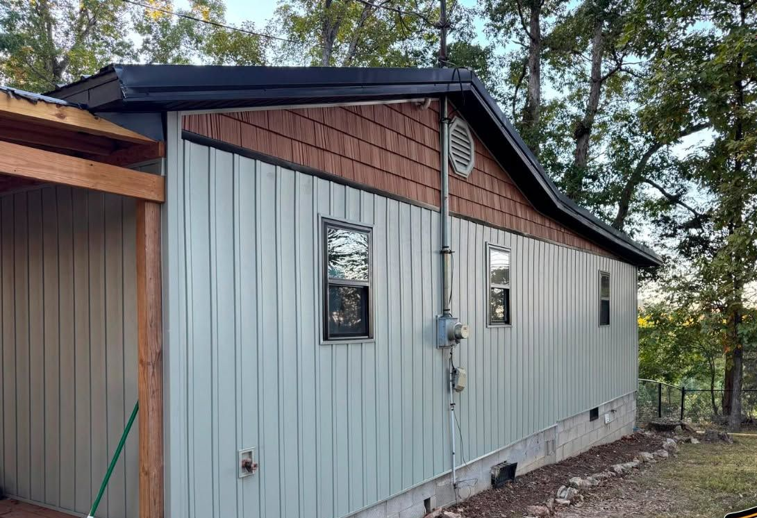 Small metal-sided building with brown roof and windows among trees on a wooded lot