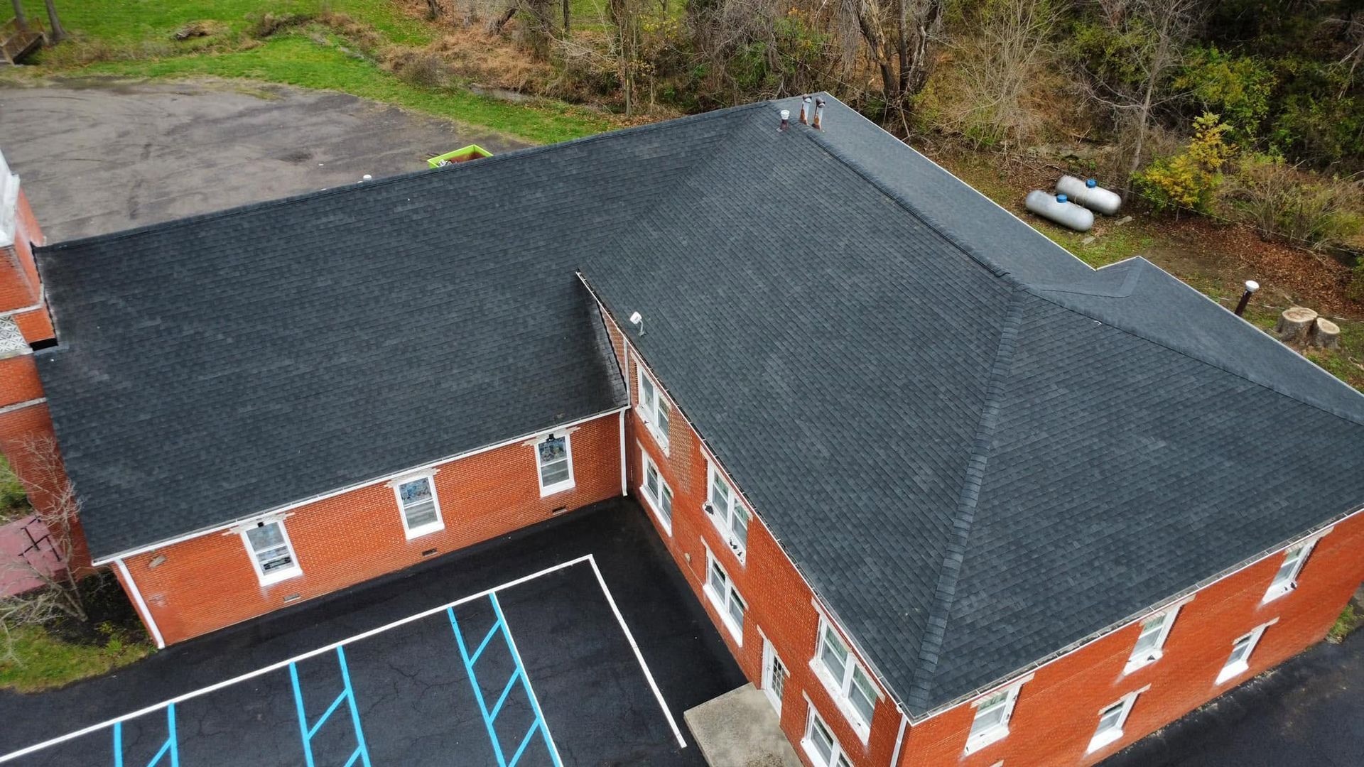 Aerial view of a red brick building with a dark roof and empty parking lot markings.