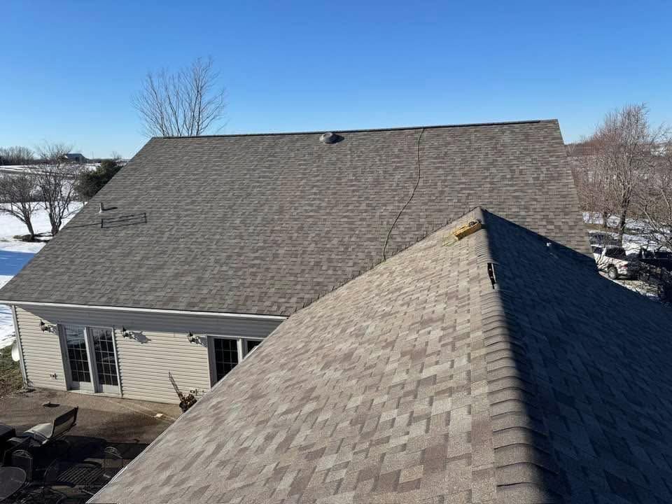 Aerial view of a house roof with gray shingles and a snow-covered yard in the background