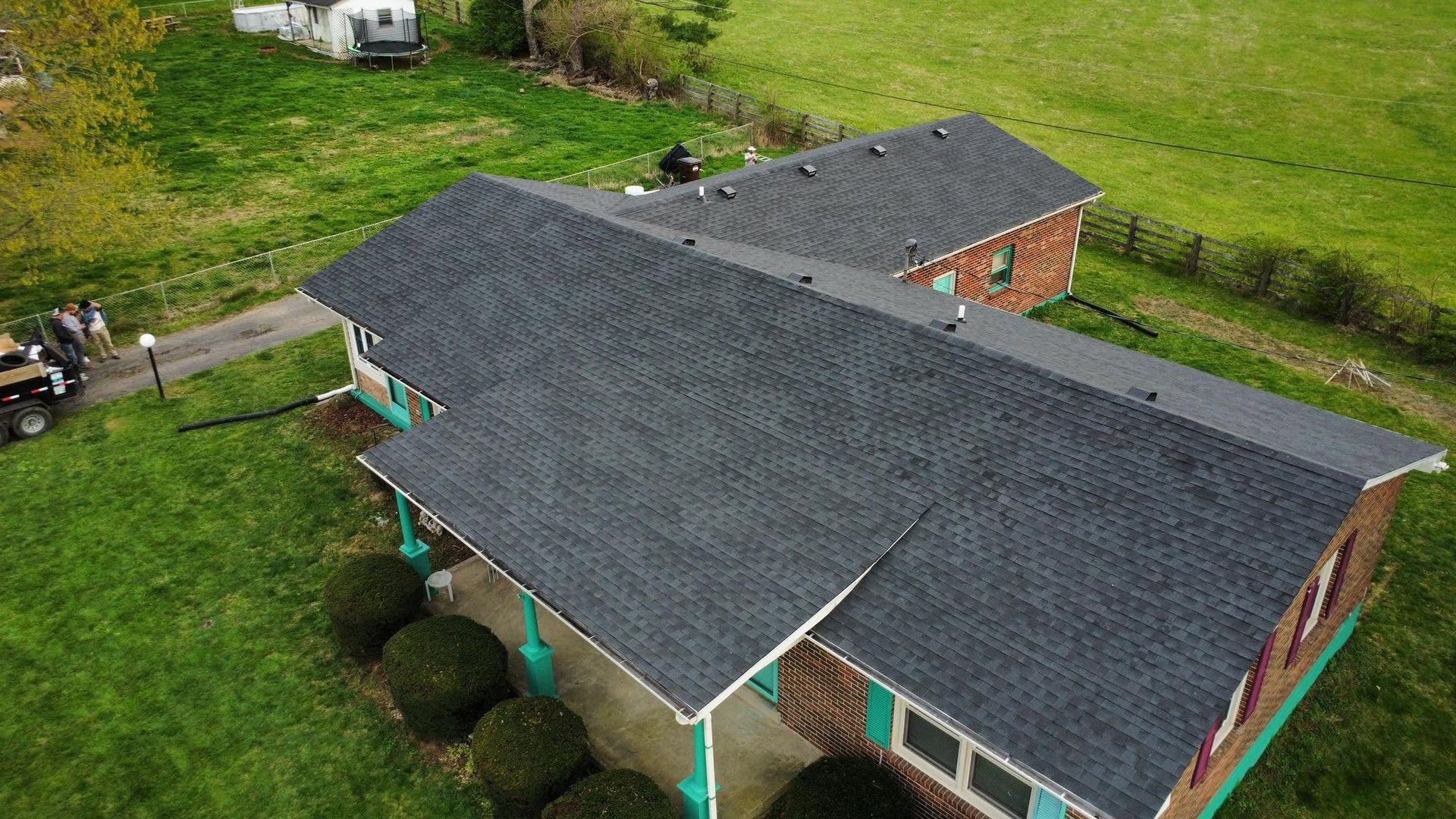 Aerial view of a house with a dark gray roof, red brick walls, and green lawn surrounding it.