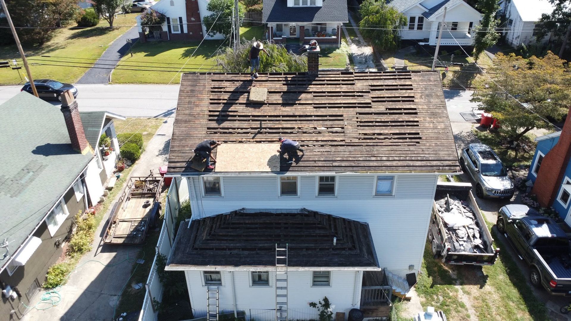 Aerial view of a house roof under repair, with exposed wooden decking and workers on top.