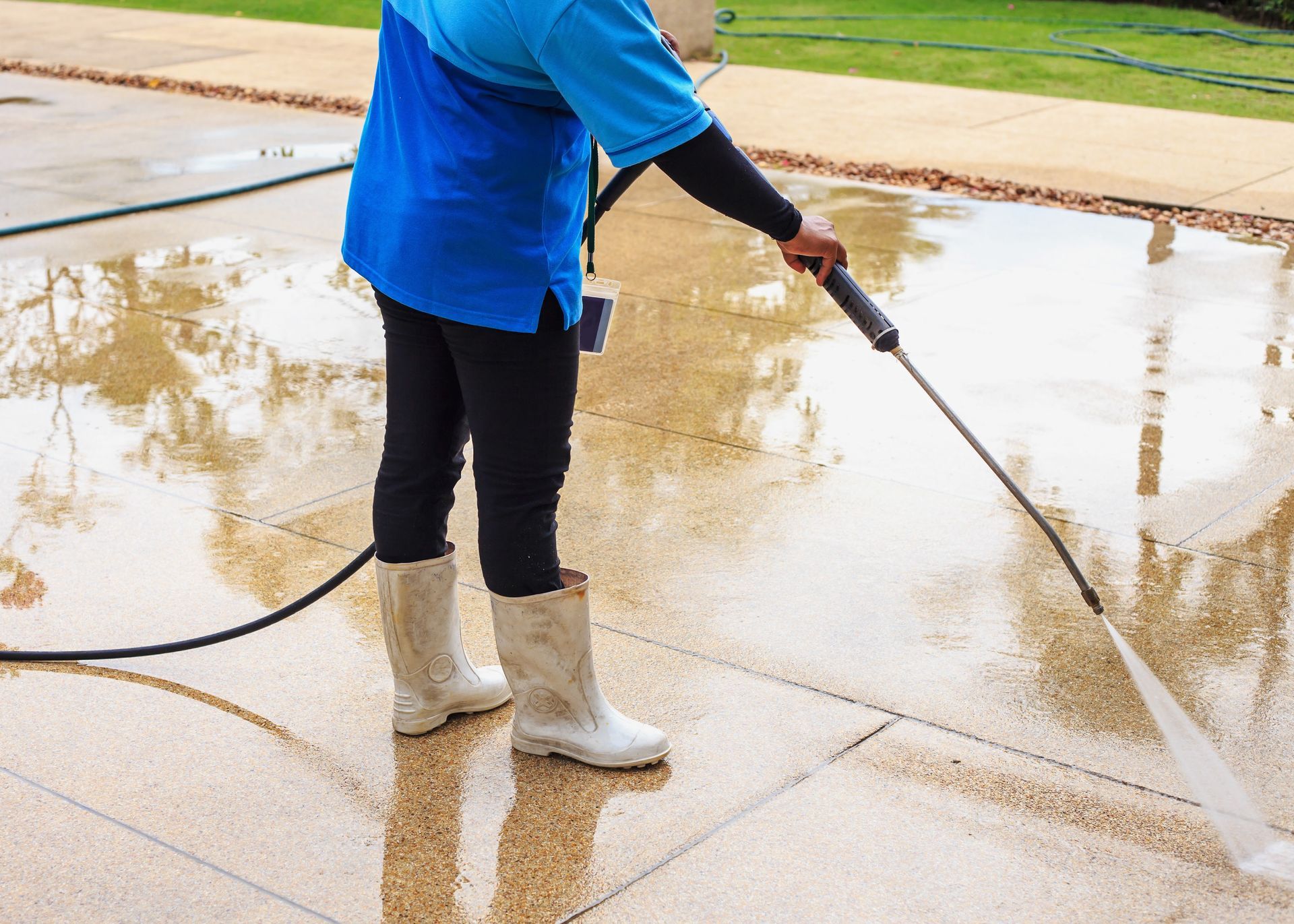 Person in blue shirt power-washing a wet concrete surface outdoors