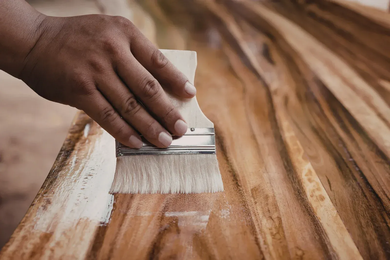 Hand using a brush to apply white finish to a wooden surface