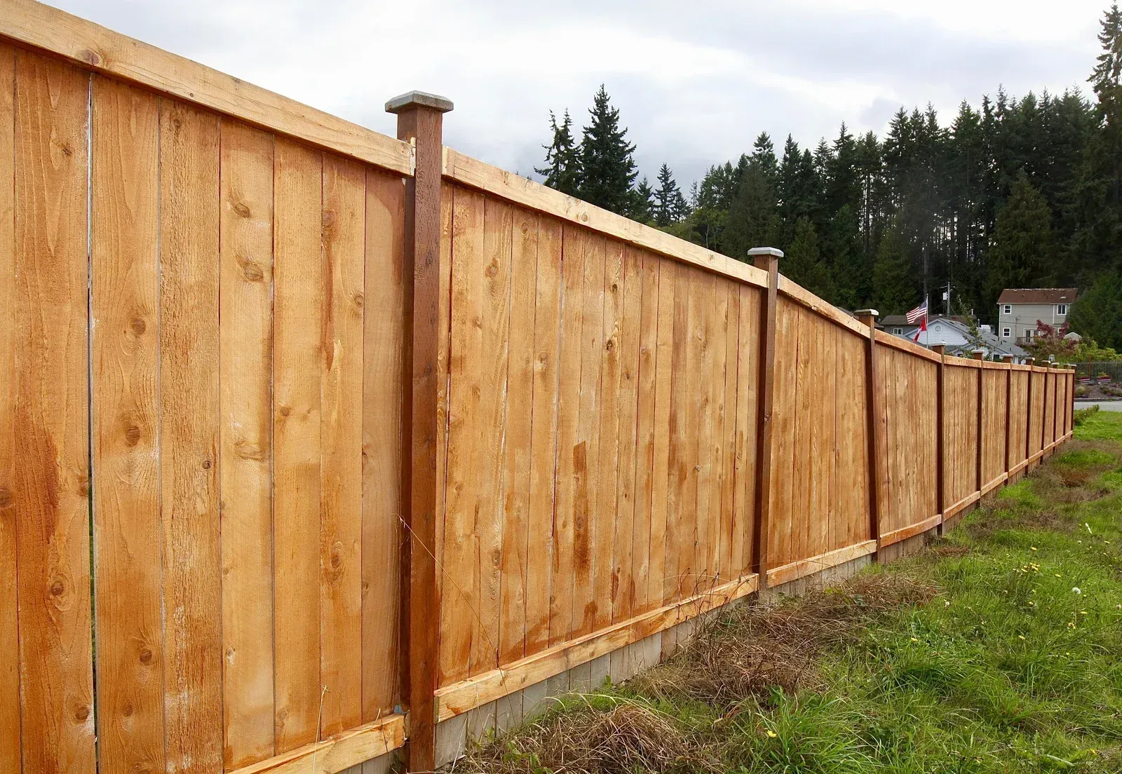 Long wooden fence with posts along a grassy yard beside a wooded area