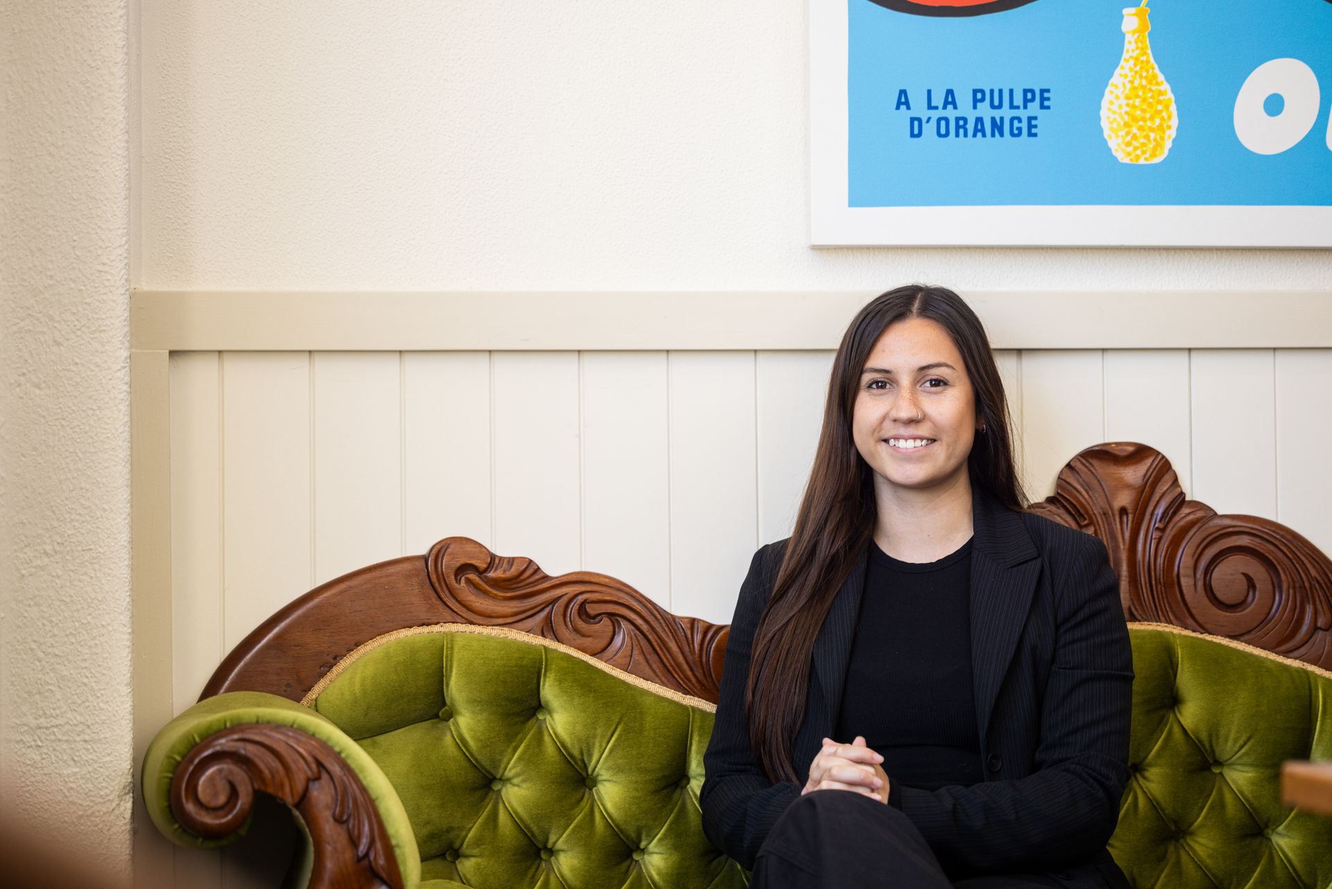 Woman seated on a green velvet sofa in front of a wall with a blue sign.