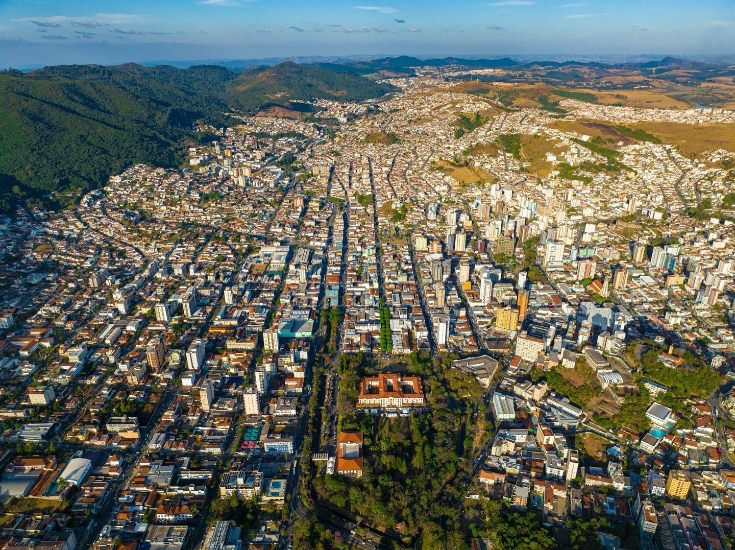 Vista aérea de uma cidade densa com ruas em forma de grade, prédios e colinas verdes ao fundo, sob um céu azul.imperador hotel