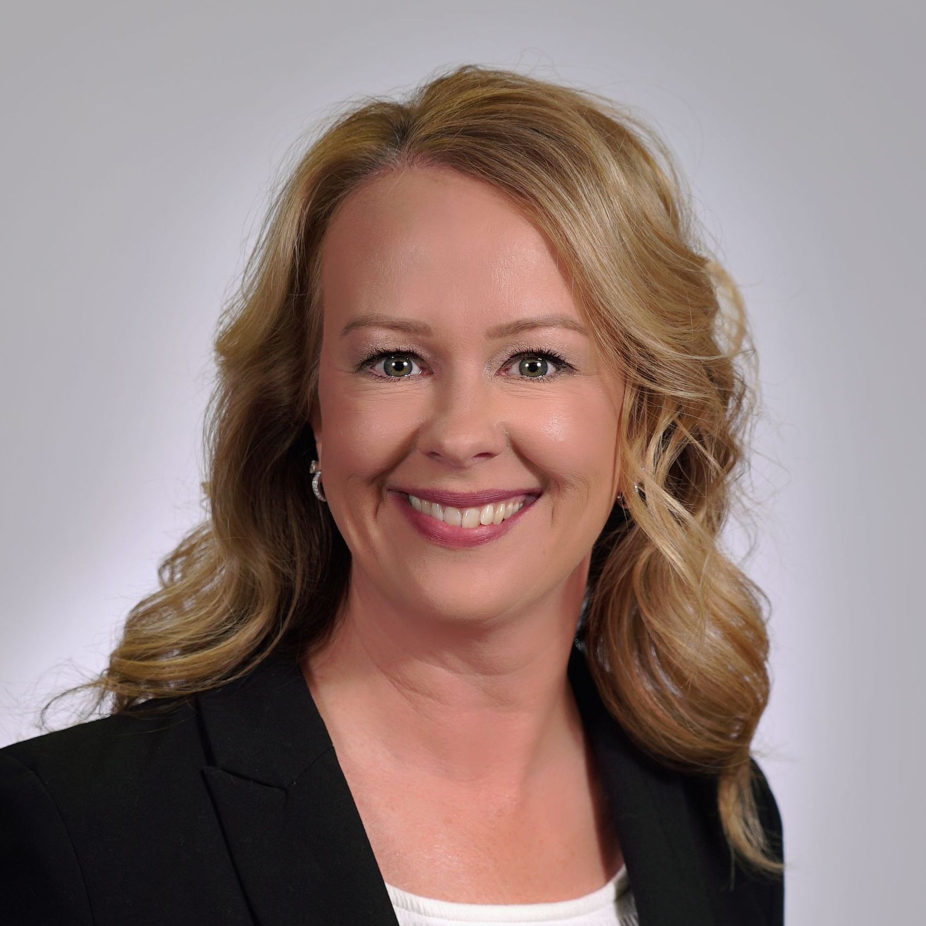 A woman in a black jacket and white shirt is smiling for the camera.