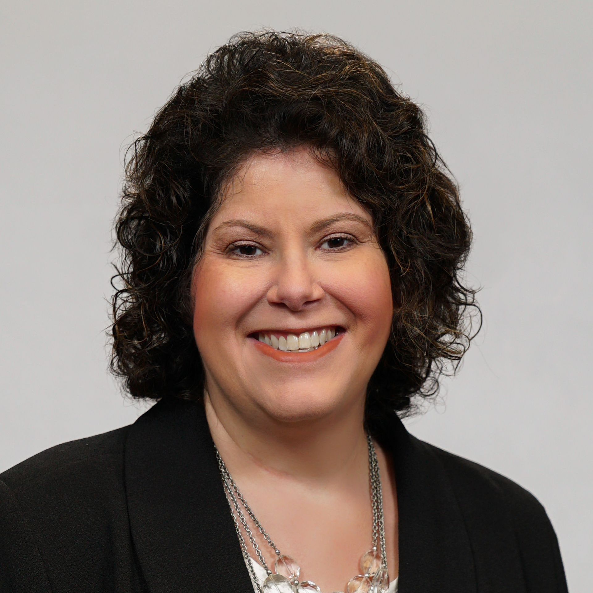 A woman wearing a blue shirt and a black jacket is smiling for the camera.