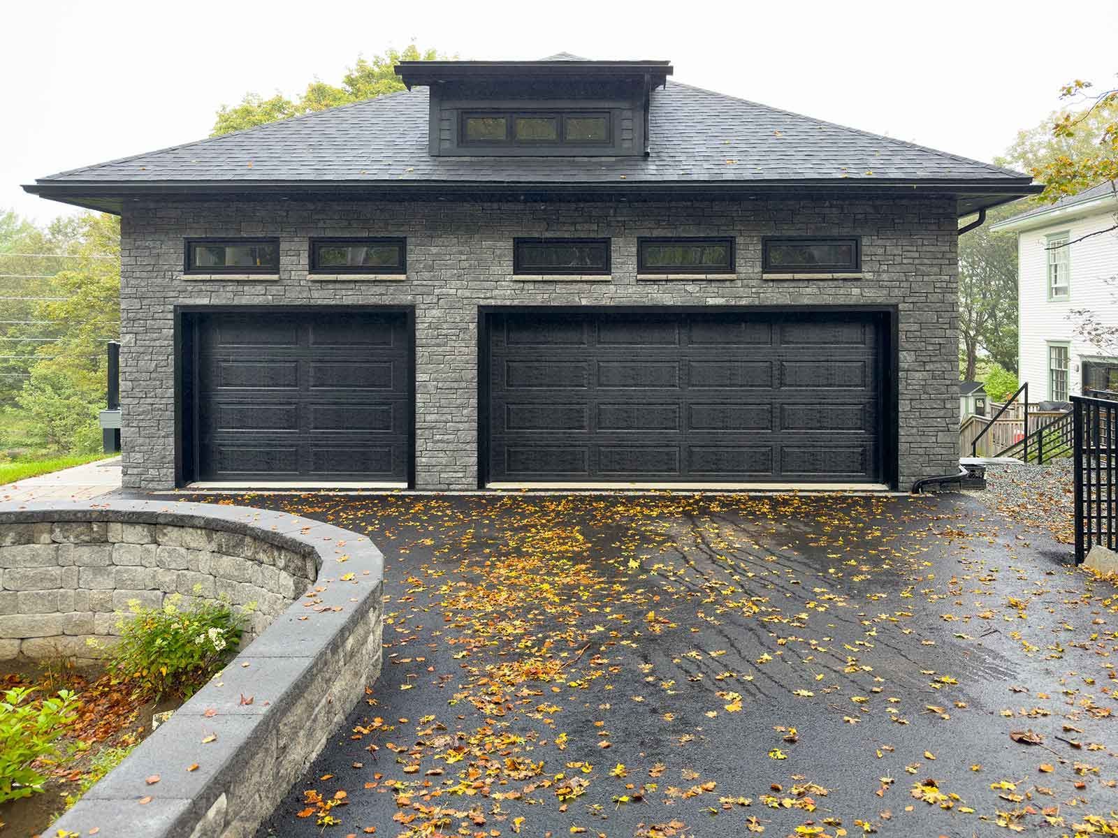 A large garage with two black garage doors and a brick wall.
