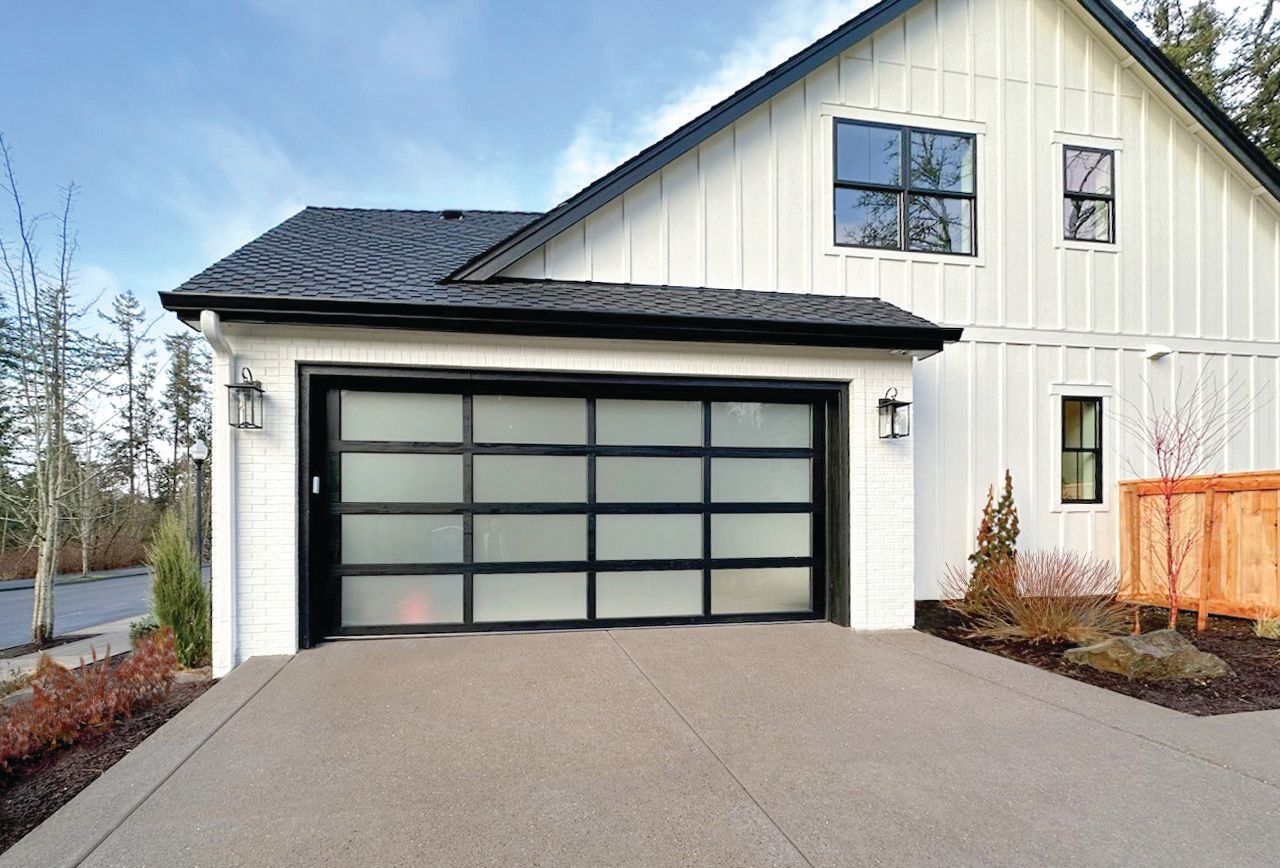 A white house with a black garage door and a driveway.
