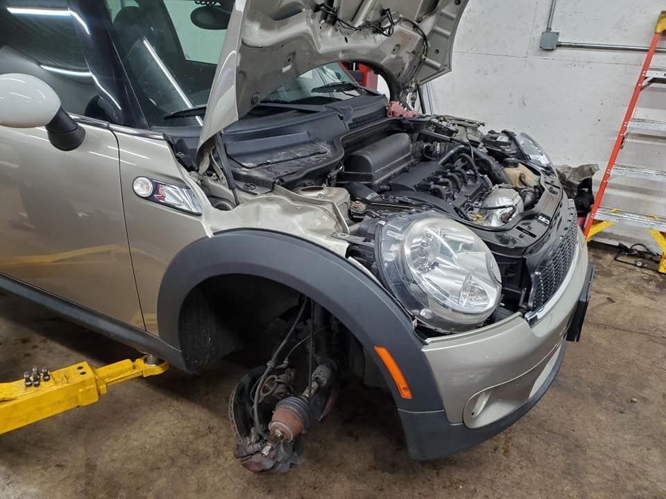 A car with the hood up is on a lift in a garage.