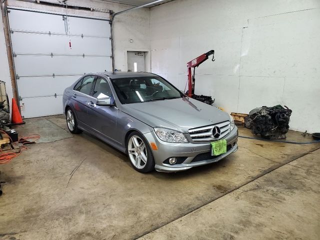 A silver mercedes benz is parked in a garage next to a crane.
