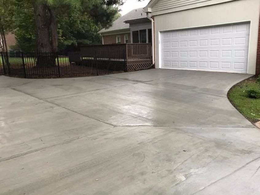 A freshly poured concrete driveway leads to a garage. A deck and fence are visible nearby.