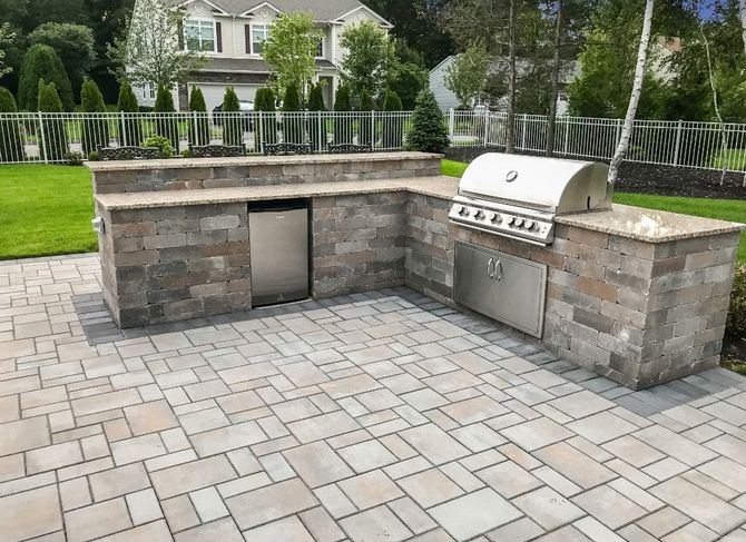 Outdoor kitchen with stone counters, grill, fridge, and matching brick patio.