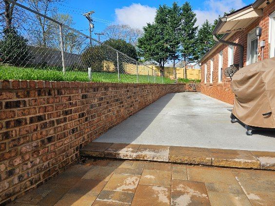Brick retaining wall beside a concrete patio. House on the right, chain-link fence in the background.