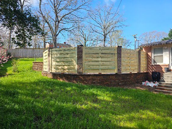 Wooden slat fence with brick pillars built on a brick base in a grassy yard.