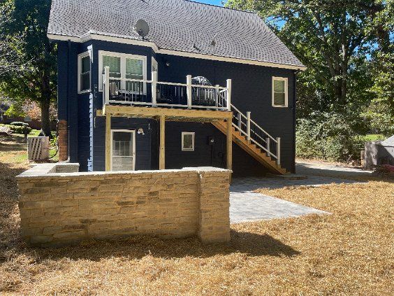 Two-story house with dark blue siding, a wooden deck, and a stone retaining wall.