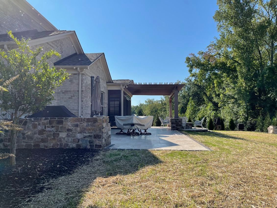 Backyard patio with pergola, brick house, and green grass on a sunny day.