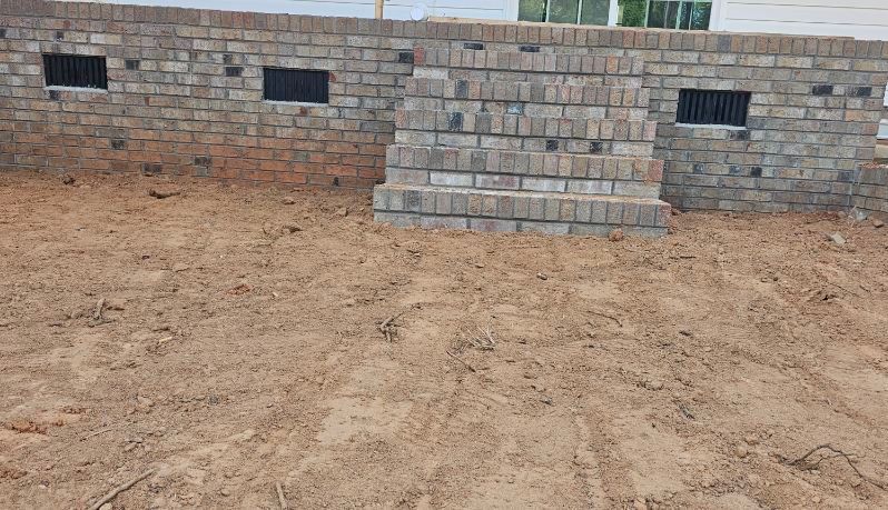Brick wall foundation with window openings and a pile of bricks on brown dirt.