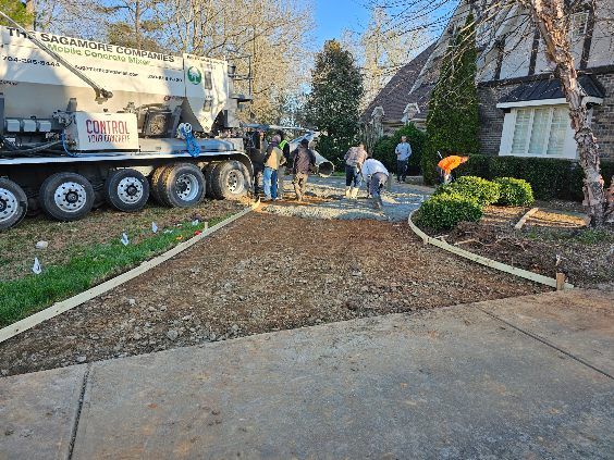 Construction crew pouring concrete for a driveway, next to a concrete truck and a house.