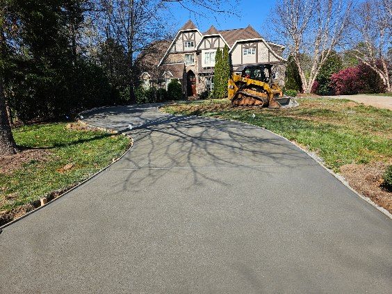 Driveway leading to a house with a skid steer parked on the grass.
