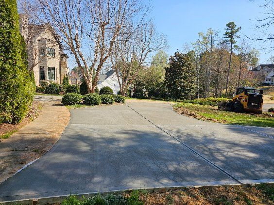 Concrete driveway curving toward a house with landscaping; small construction vehicle visible.