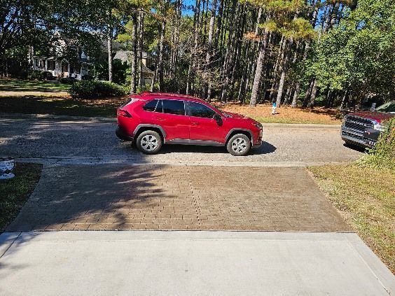 Red SUV parked on a paved driveway with a street and trees in the background on a sunny day.
