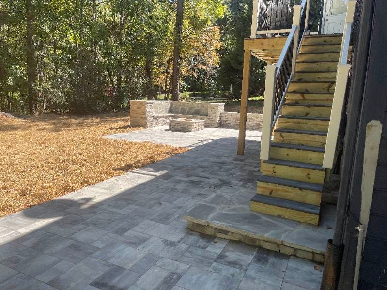 Brick patio with steps, seating area, and fire pit in a backyard setting with trees.