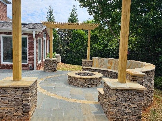 Stone patio with fire pit, built-in curved stone seating, and a wooden pergola supported by stone columns.