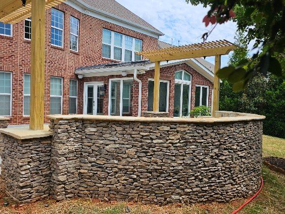 Stone retaining wall supporting a deck with pergola, attached to a brick house.