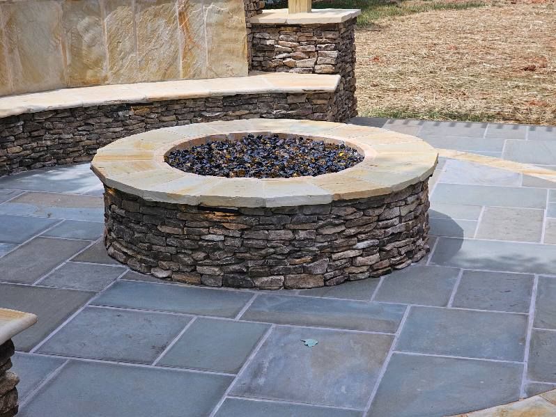 Stone fire pit and seating area on a blue-gray paved patio.