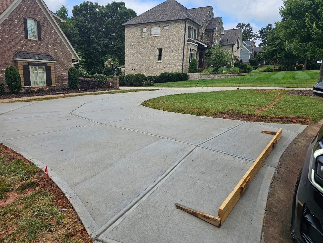 Newly poured concrete driveway with wooden level, houses, and green grass.
