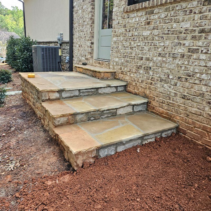 Stone steps leading to a door; steps are brown and beige against a brick wall and dirt.