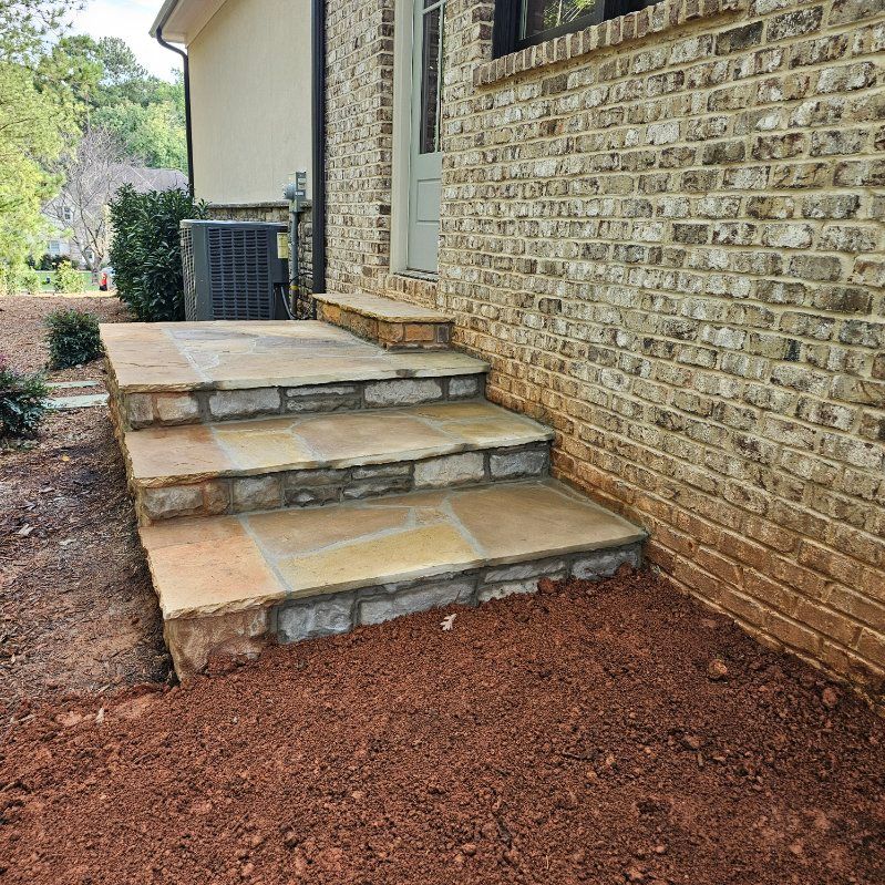 Stone steps leading up to a brick building's doorway, surrounded by reddish-brown soil.