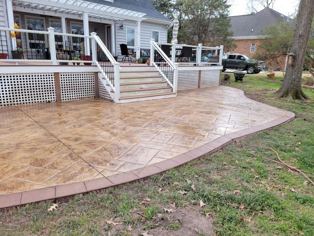 Stamped concrete patio with a house and deck in the background, surrounded by grass.