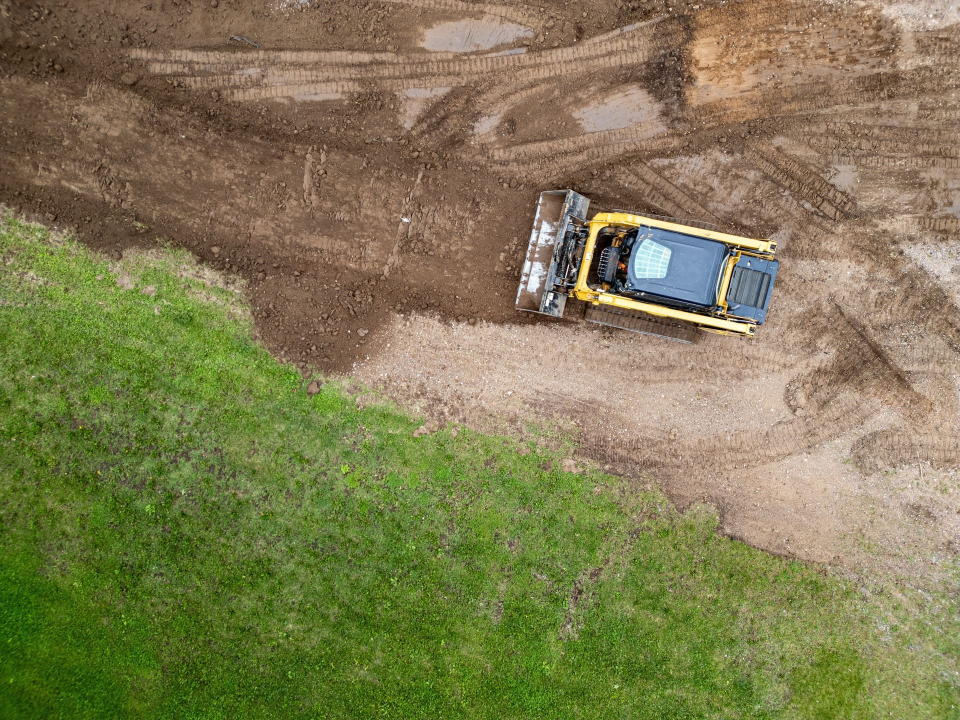 Yellow bulldozer smoothing soil near grassy area.