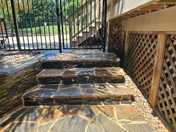 Stone steps leading up to a black metal gate and wooden lattice, outdoors in sunlight.