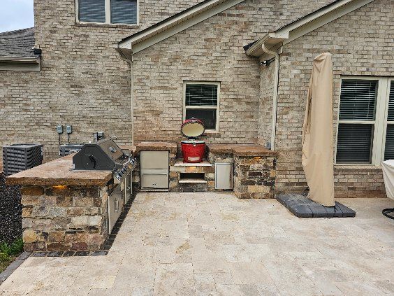 Outdoor kitchen with brick facade and stone countertops. Features grill, cabinets, and a red smoker.