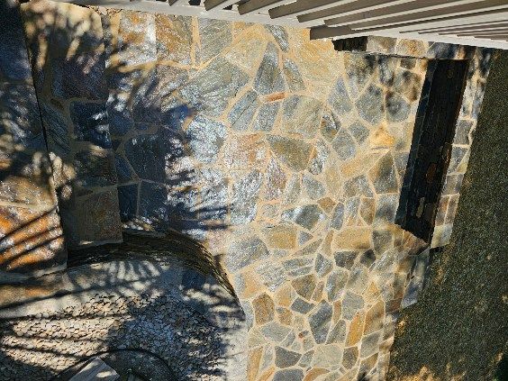 Stone patio with shadows cast by trees, partially under a covered structure.