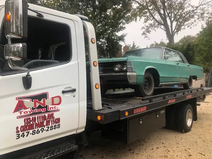 A teal vintage car is being towed by a white tow truck.