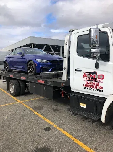 Blue BMW sports car on a flatbed tow truck in an outdoor setting.