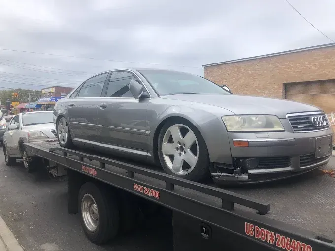 Silver Audi sedan on a flatbed tow truck, damaged front bumper, parked on a city street.
