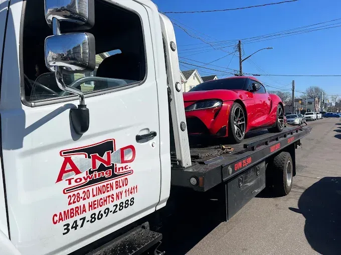 Red Toyota Supra being towed by a white tow truck on a sunny street.