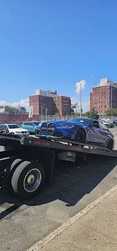 A blue sports car being transported on a flatbed tow truck on a sunny day.