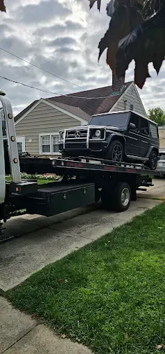 Black Mercedes-Benz G-Wagon on a tow truck in front of a house.