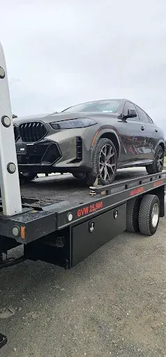 Dark-colored BMW SUV on a flatbed tow truck. Gray sky background.