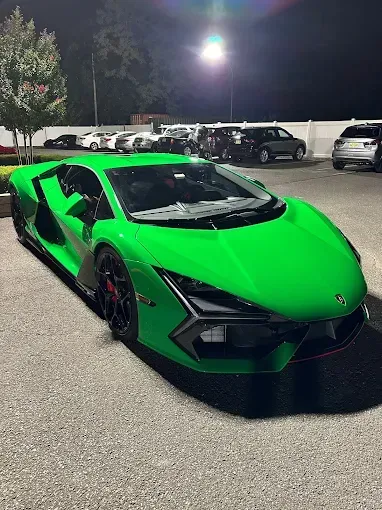 Green Lamborghini parked at night in a lot with other vehicles.