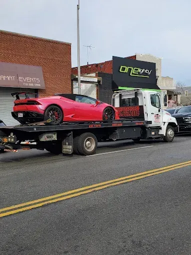 Pink Lamborghini convertible towed on a flatbed truck on a street.