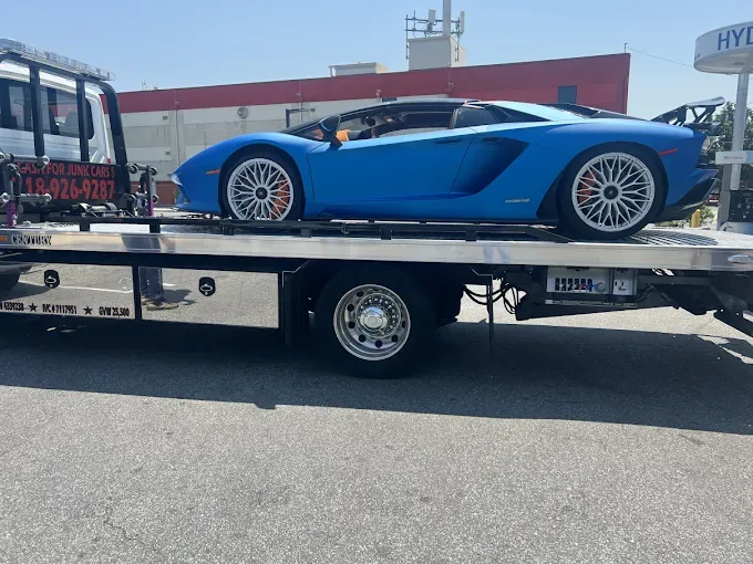 Blue Lamborghini convertible on a tow truck, likely being transported.