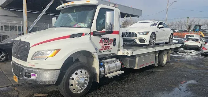 White tow truck carrying a white car, parked outside.